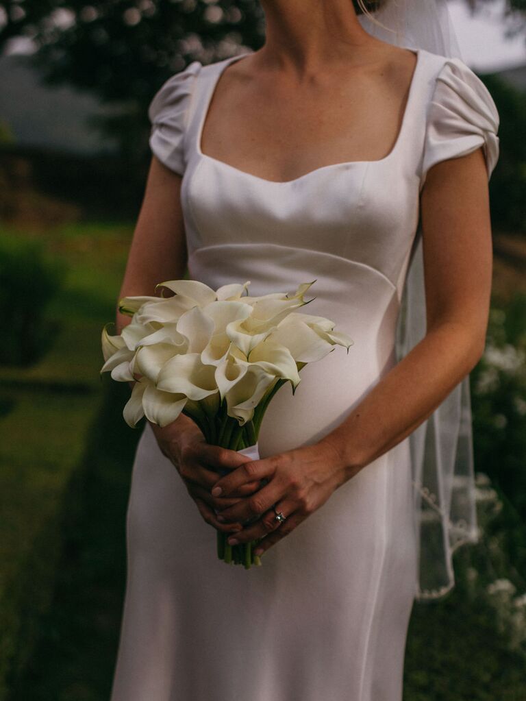 2023 wedding flower trend bride holding simple wedding bouquet of white calla lilies