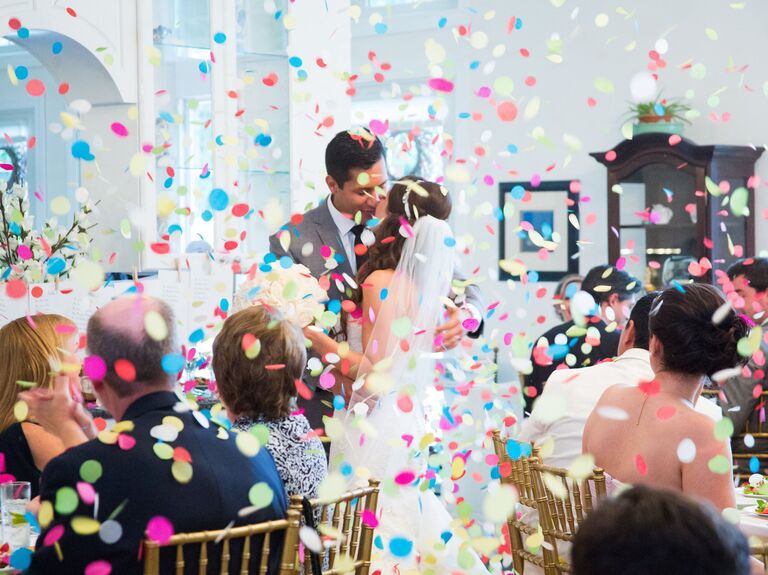 Bride and groom standing in a colorful confetti shower. 