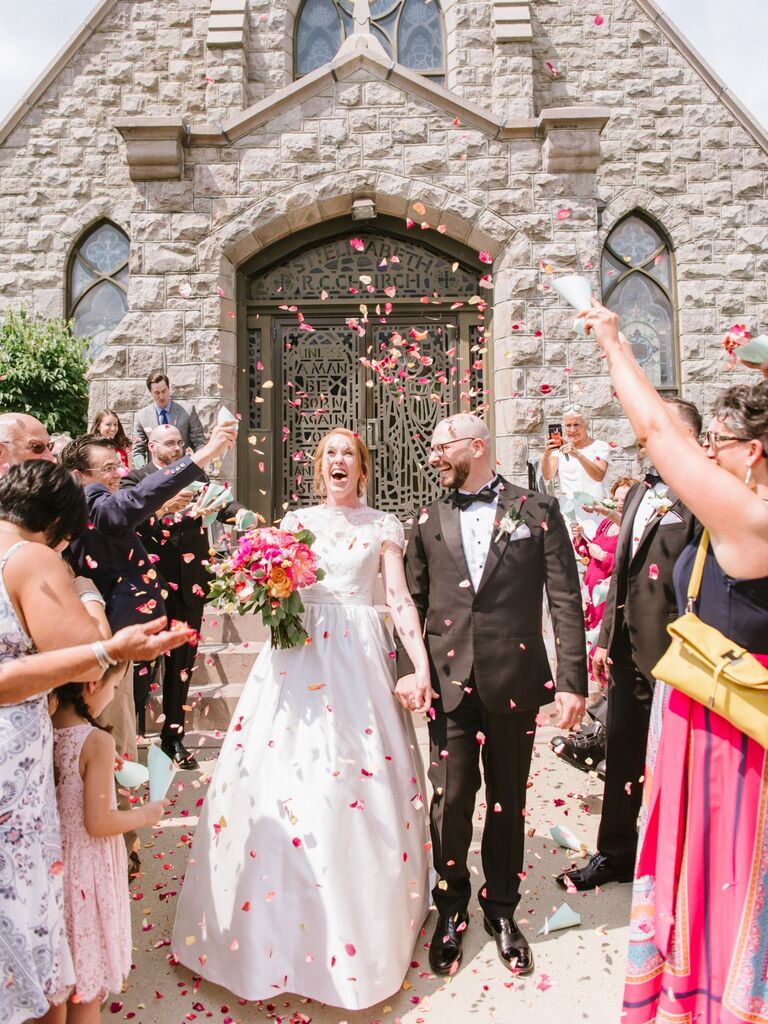 Couple leave their wedding ceremony while guests throw flower petals. 