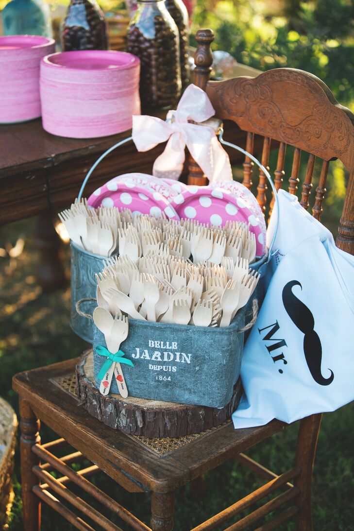 Beige colored plastic utensils were organized inside gray buckets with pink and white polka dotted plates. Theres were used to eat ice cream from the dessert and coffee table.