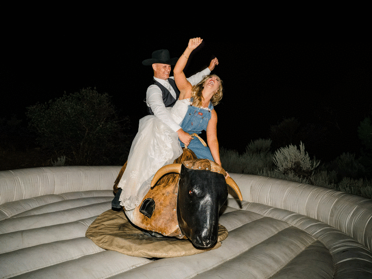 Bride and groom ride mechanical bull as a first dance alternative.