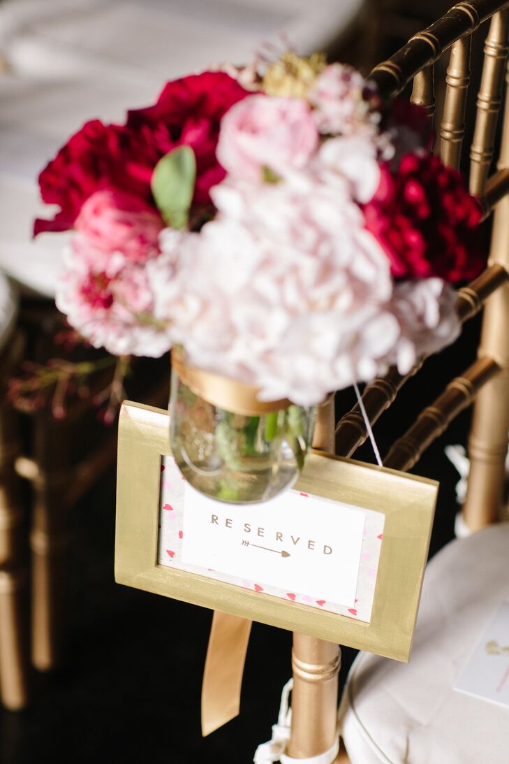 Simple gold frames popped against chiavari chairs in the same hue. For an added pop of color, red and pink arrangements of hydrangeas and garden roses lined the aisle.