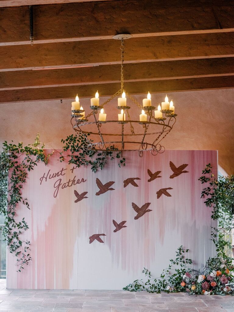 Pastel pink backdrop with bird details underneath chandelier