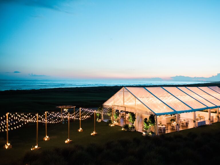 aerial view of clear top wedding reception tent at night with string lights illuminating the path to the tent