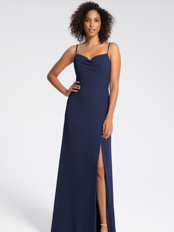 A model wears a navy blue dress with a cowl neckline, spaghetti straps, and a slit.
