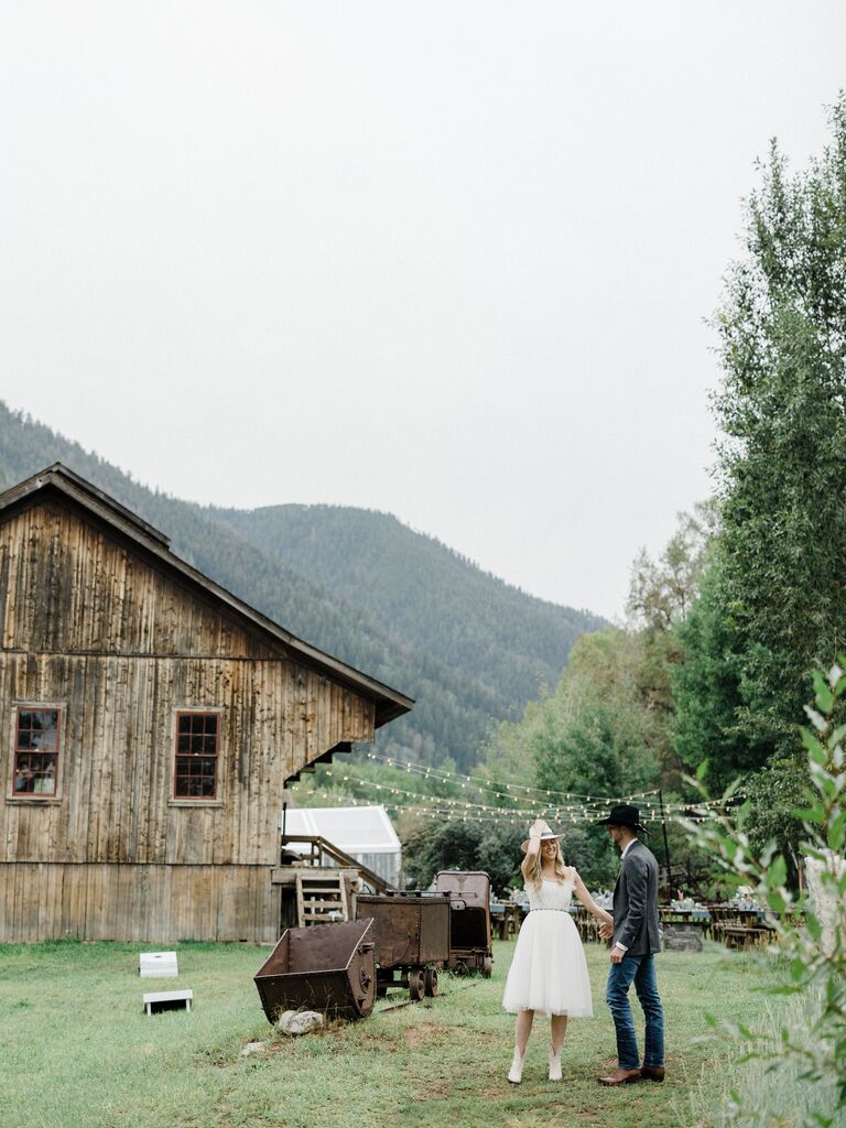A couple stand together in the foreground of this rustic engagement photo
