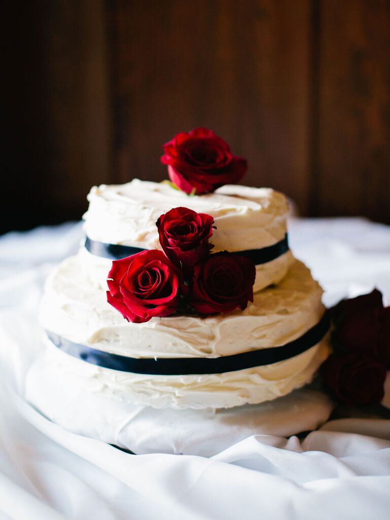Small two-tier wedding cake with white buttercream frosting and black ribbons and red roses