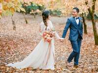 bride and groom holding hands walking through forest of orange trees in fall