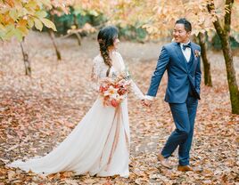 bride and groom holding hands walking through forest of orange trees in fall