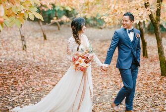 bride and groom holding hands walking through forest of orange trees in fall