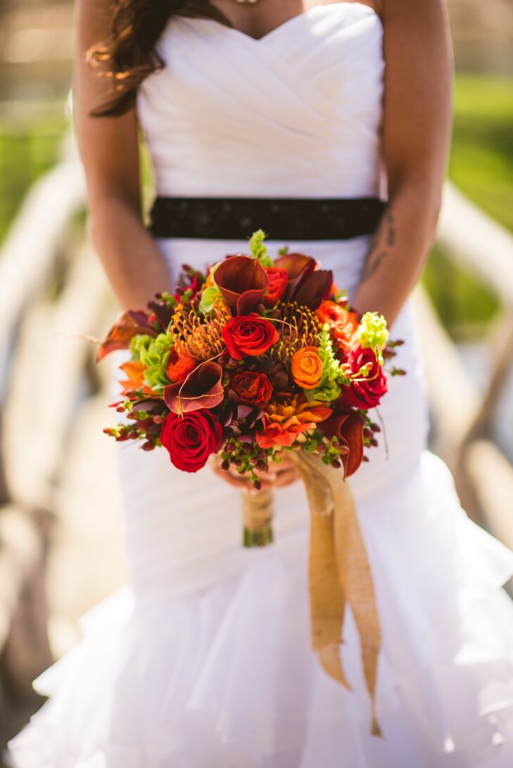 Their favorite flower, the mango calla lily, popped up in arrangements throughout the wedding, including Ashley’s bouquet. She worked with Ibranyi Is Floral to fill it with earth-tone-inspired flowers. Red orange and crimson roses, orange and red ranunculus, orange dahlias, red hypericum berries, orange proteas, greenery and, of course, their calla lilies were all put in the bouquet and wrapped in burlap.
