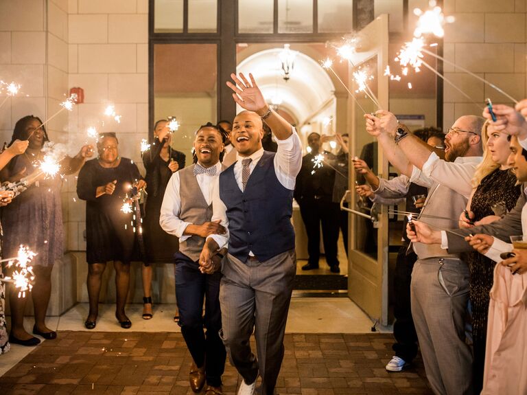 Grooms wave at guests during sparkler wedding exit. 