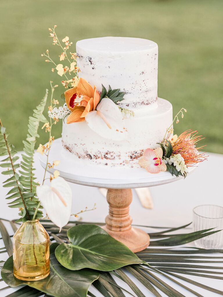 two tier white wedding cake with orange orchids and tropical greenery