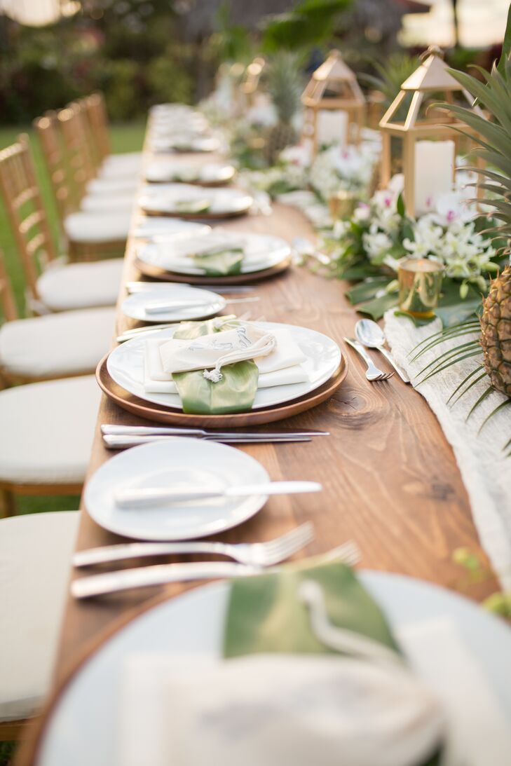 At the reception at the Four Seasons Resort Maui in Wailea, Hawaii, a long wooden banquet table was topped with simple white plates as well as fern fronds, lanterns and pineapples.