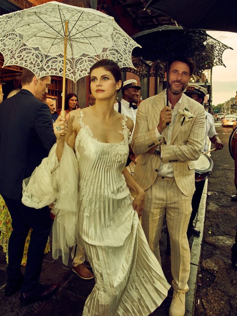Alexandra Daddario wears a chic white dress and holds a lace parasol. 