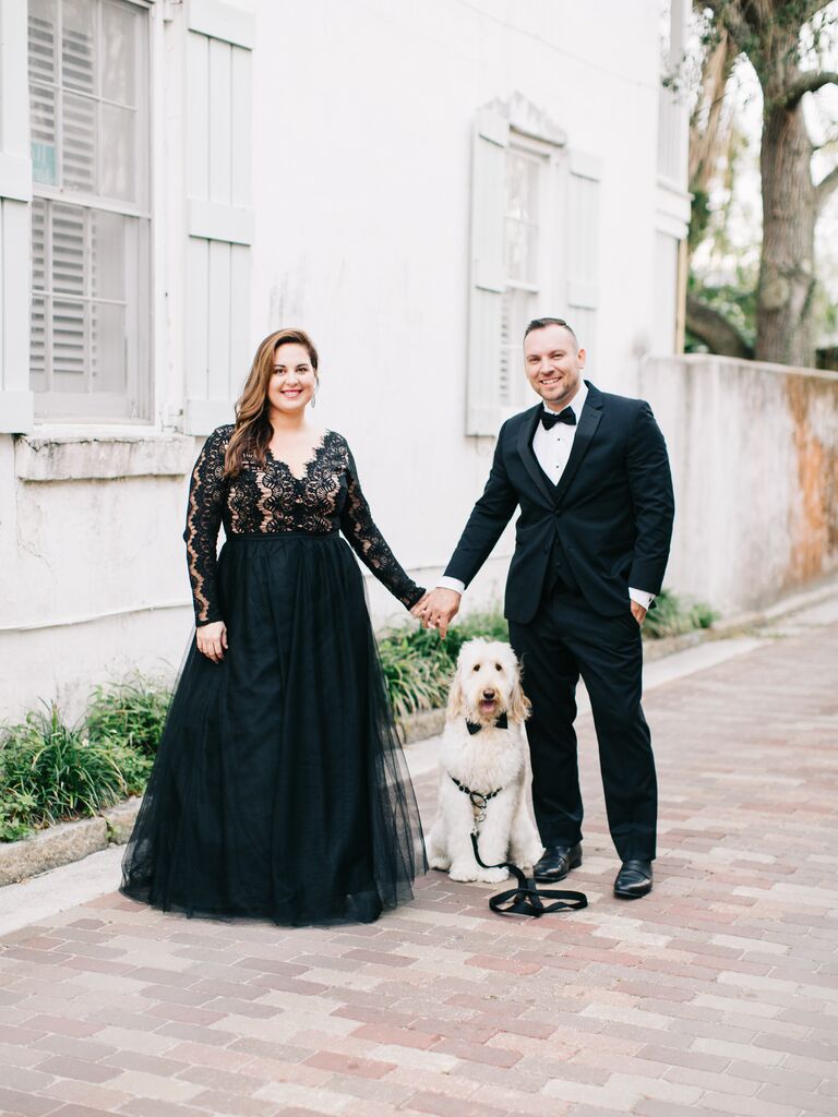 Bride and groom holding hands and posing with their dog.