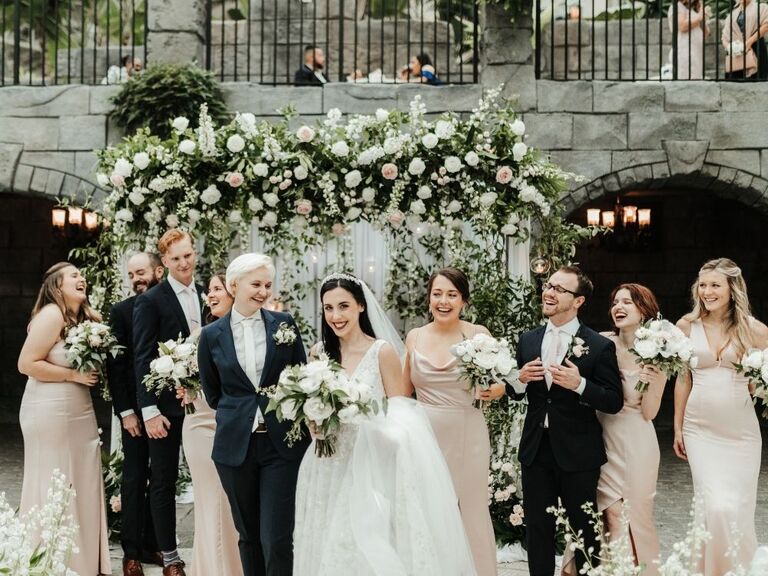 brides posing with wedding party members at greenery-covered ceremony altar