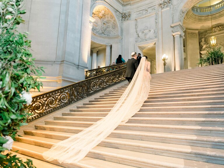 bride wearing 20 foot royal wedding veil walks up the marble staircase at san francisco city hall wedding ceremony