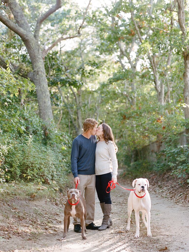 Happy couple kissing while holding their two dogs on a leash.