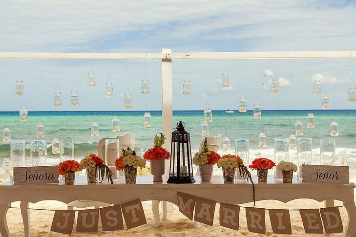 "Senor" and "Senora" signs marked Marta and Jose Luis's beachfront sweetheart table, lined with coral and white potted blooms. Hanging votives enhanced the romance of the beach backdrop.