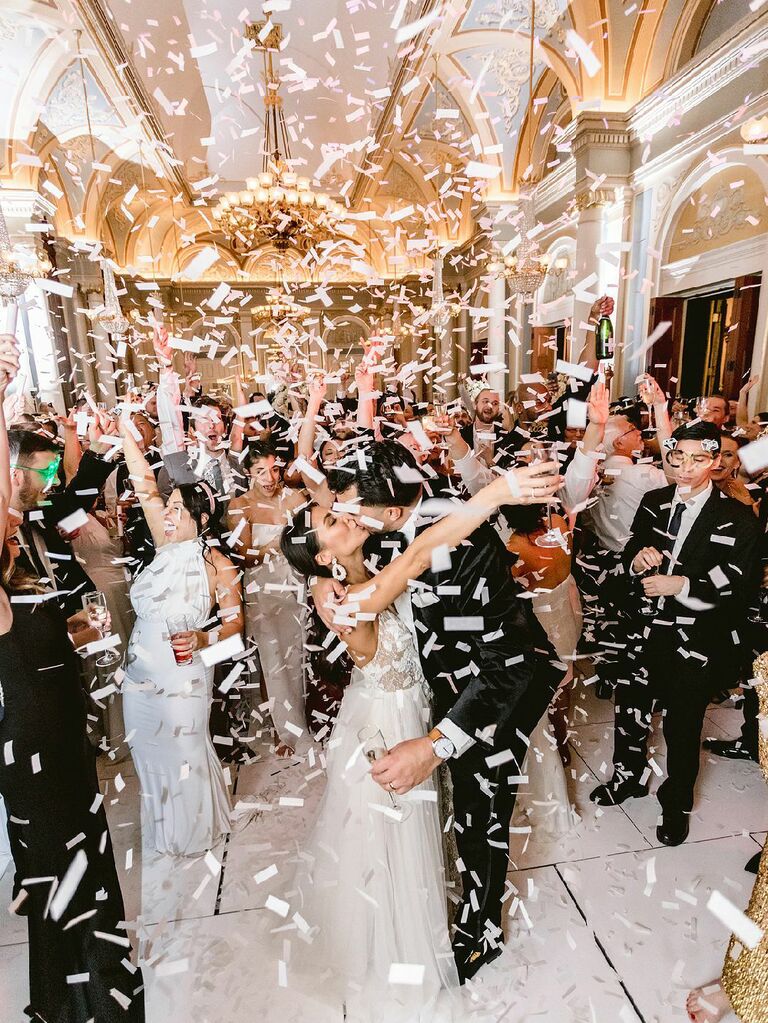 Bride and groom kissing under confetti shower at wedding reception