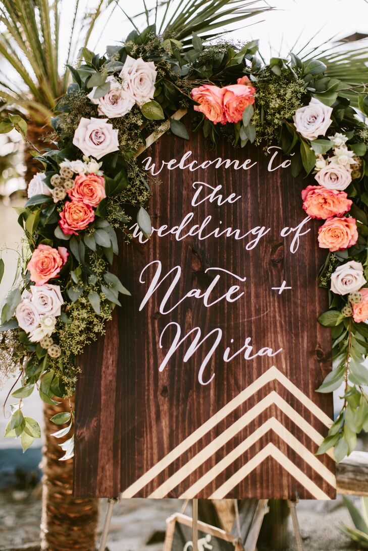 Sunset-hued floral garlands were used throughout the event. Here, one is draped over a wooden welcome sign.