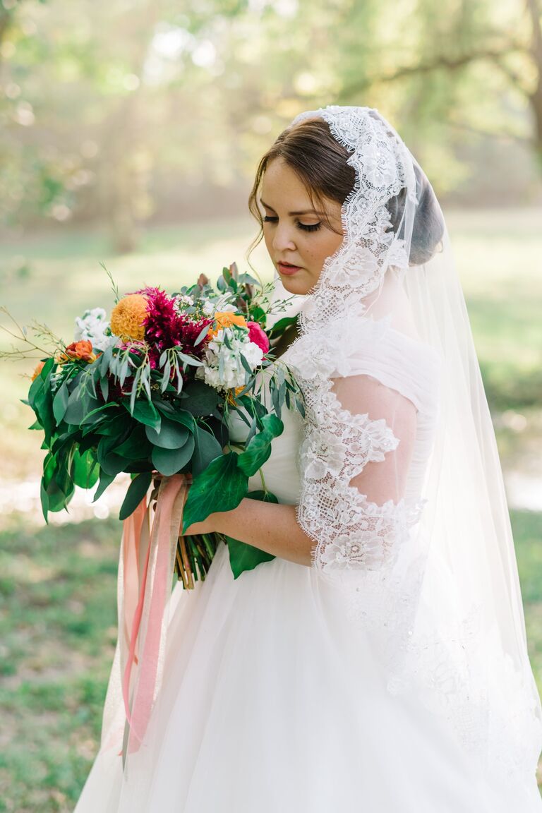 bride holds her wedding bouquet wearing a lace trimmed mantilla veil with updo