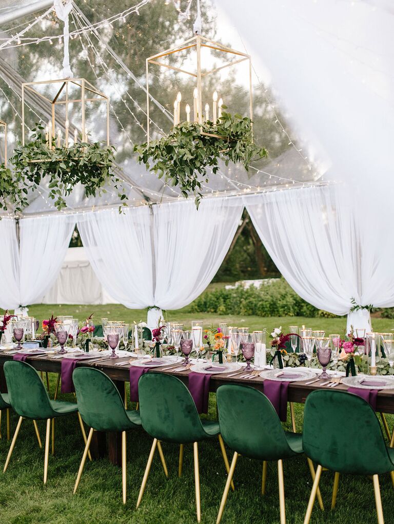 Gold chandeliers with candles inside raised above reception tables at tented wedding