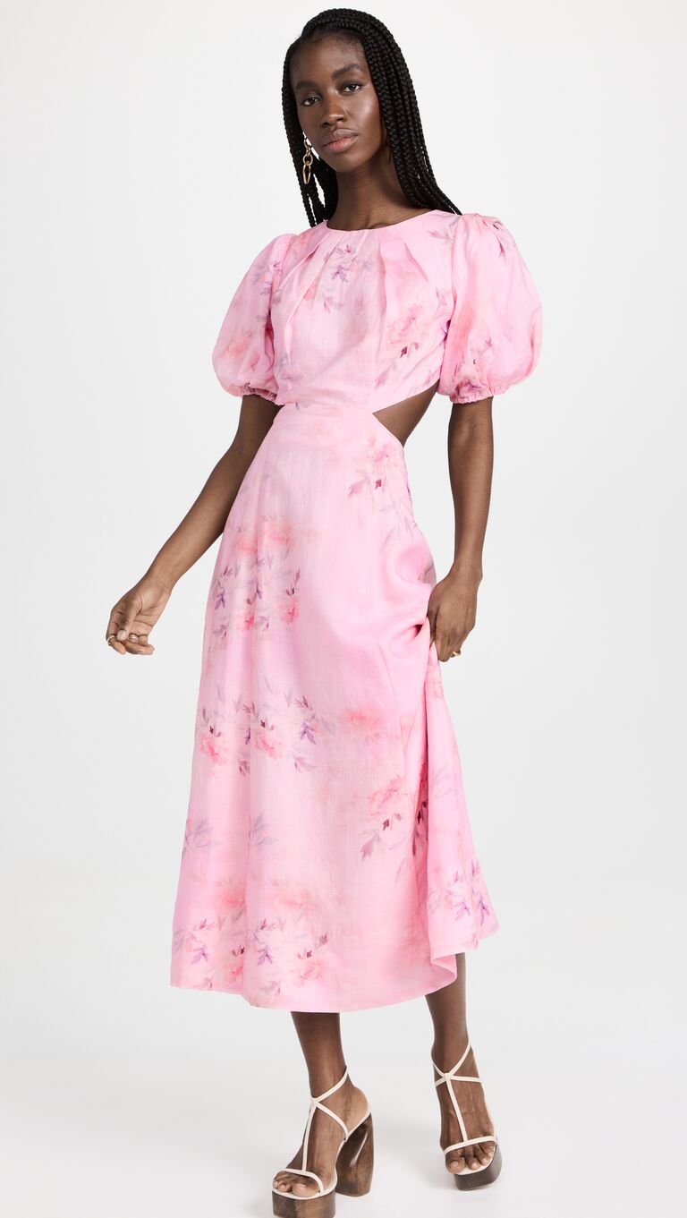 Model wears a pink dress with cutouts at the waist and puffy sleeves. 