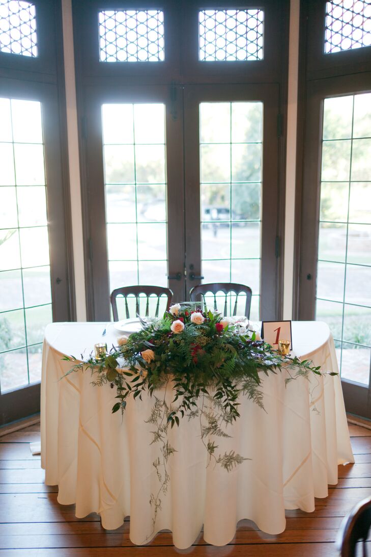 Windermere Flowers and Gifts brought out the couple's bright wedding colors with a tablescape of eucalyptus, orange roses, red garden roses and greenery that cascaded over the sweetheart table's its champagne linen. The lush display on added a natural touch to their decor.