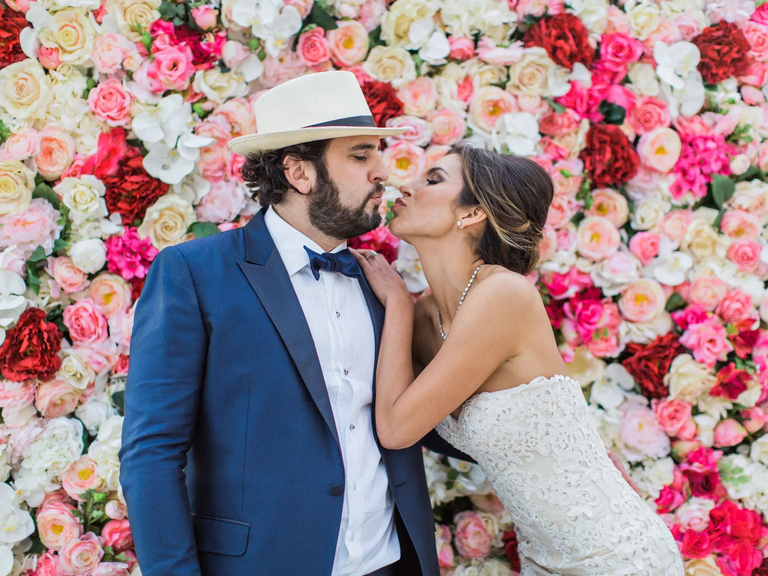 Bride and groom kiss in front of wedding flower wall photo booth.