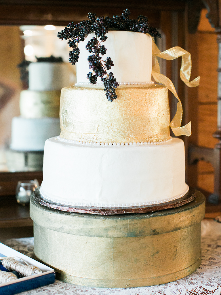 Three tier wedding cake with a black berry accent and gold buttercream 