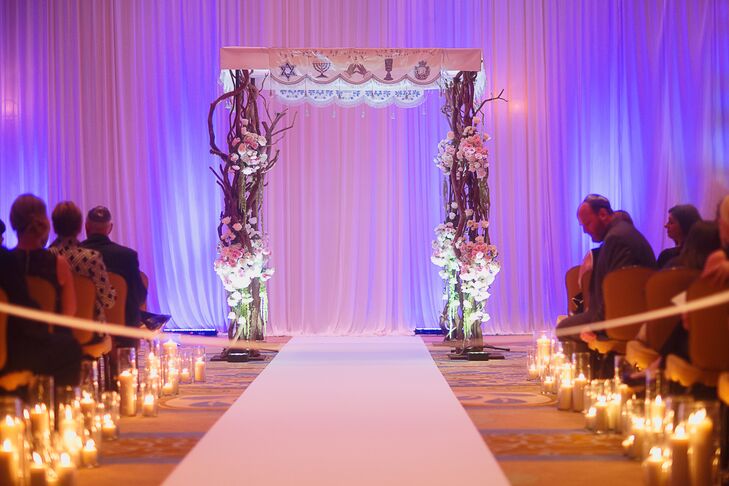 Originally, the ceremony was supposed to be outside, but, due to weather, they had to pull it inside. Despite the last-minute change, the ceremony was decorated with ivory drapery, amber lighting and lush flowers with lit pillar candles framing the aisle.