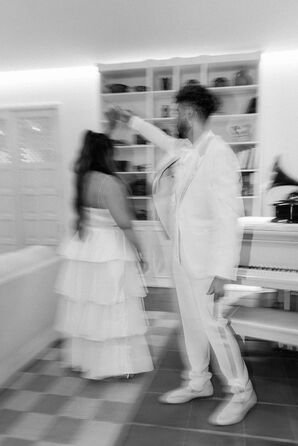 Black-and-White Action Photo of Groom in White Suit Twirling Bride
