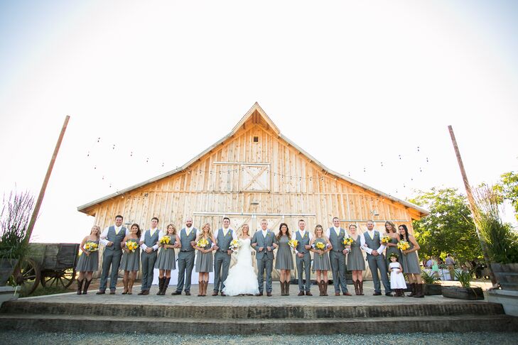 Lauren and Drake stood outside with their wedding party in a line, all wearing charcoal gray attire to match the day's color scheme. The bridesmaids wore charcoal gray knee-length dresses in different styles, while the groomsmen matched their look with gray suits.