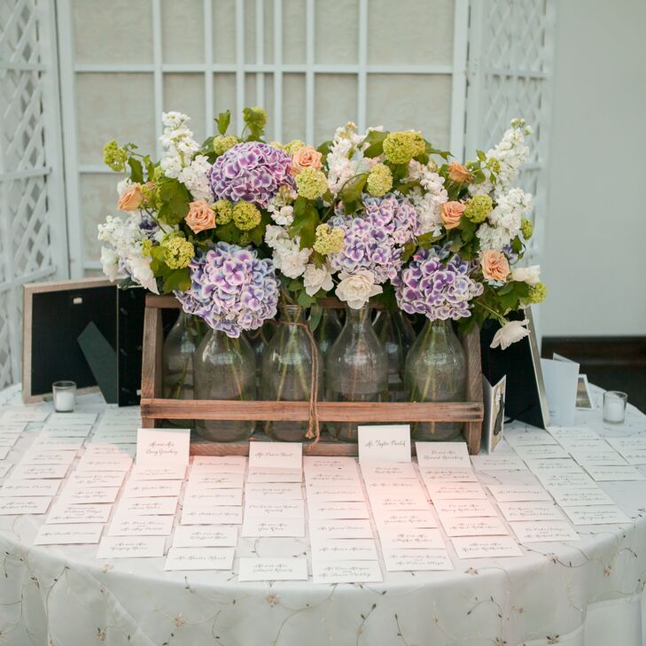 On the place card table, Alexandra and Will's florist, Rebecca Shepherd Floral Designs, created a unique flower arrangement using glass vases of purple, coral and white roses, hydrangeas and stock and placing them in a wooden milk crate.