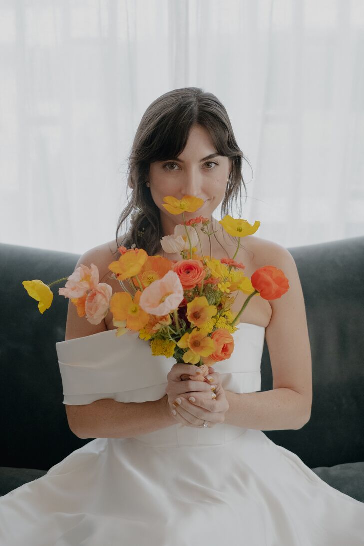 A bride in an off-the-shoulder, retro-inspired gown holding a colorful bouquet of flowers inspired by a 1970s palette of orange, pink, yellow and coral.