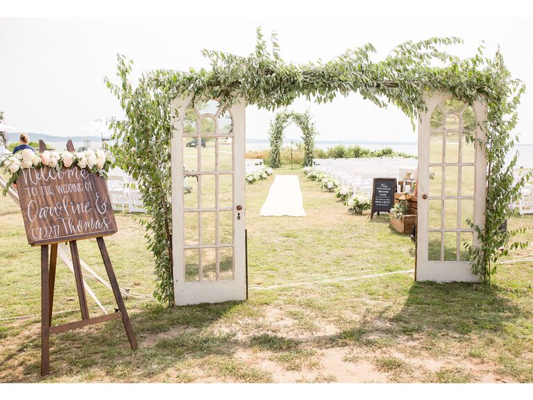 Vintage distressed French door archway covered in greenery leading to ceremony aisle