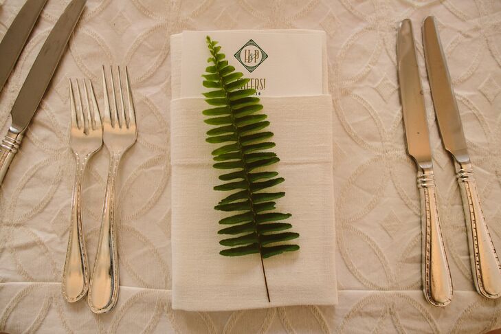 The dining tables at the reception were dressed in white tablecloths and had white napkins at each setting, which had a menu folded inside. A single fern leaf accented each napkin and menu, which represents Hailey's love for the plant that accented the decor throughout the wedding day.