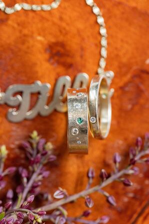 Two Gold Wedding Bands With Small Diamonds and Green Gem Embedded
