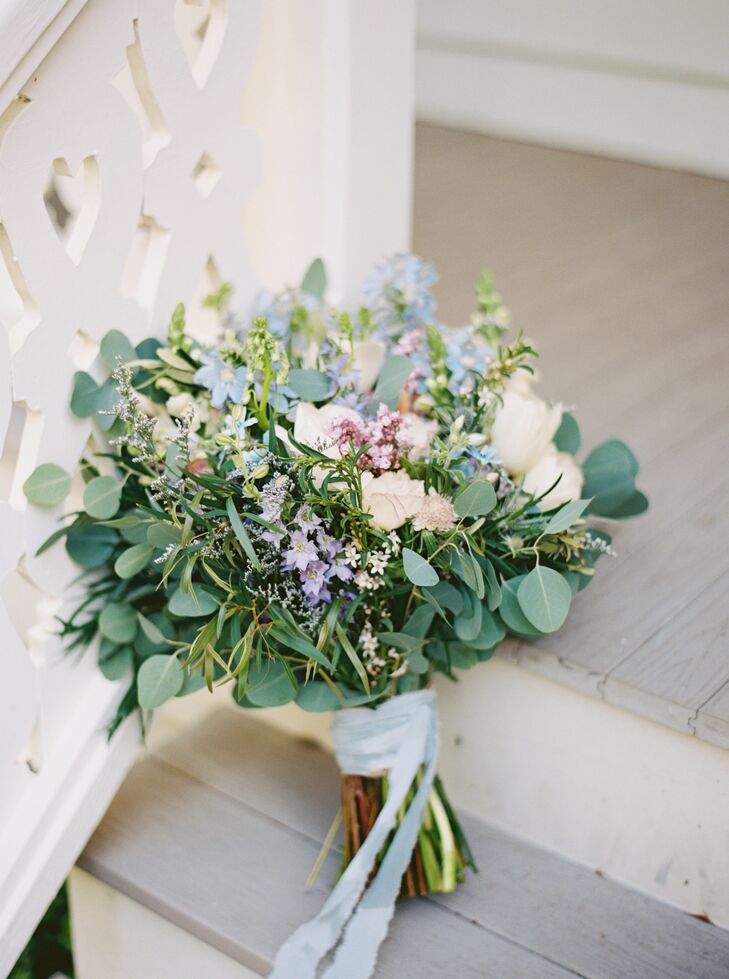 A bride's bouquet for a garden party morning wedding, featuring a natural and soft vibe with pastel colors, tons of greenery, and a delicate blue ribbon.
