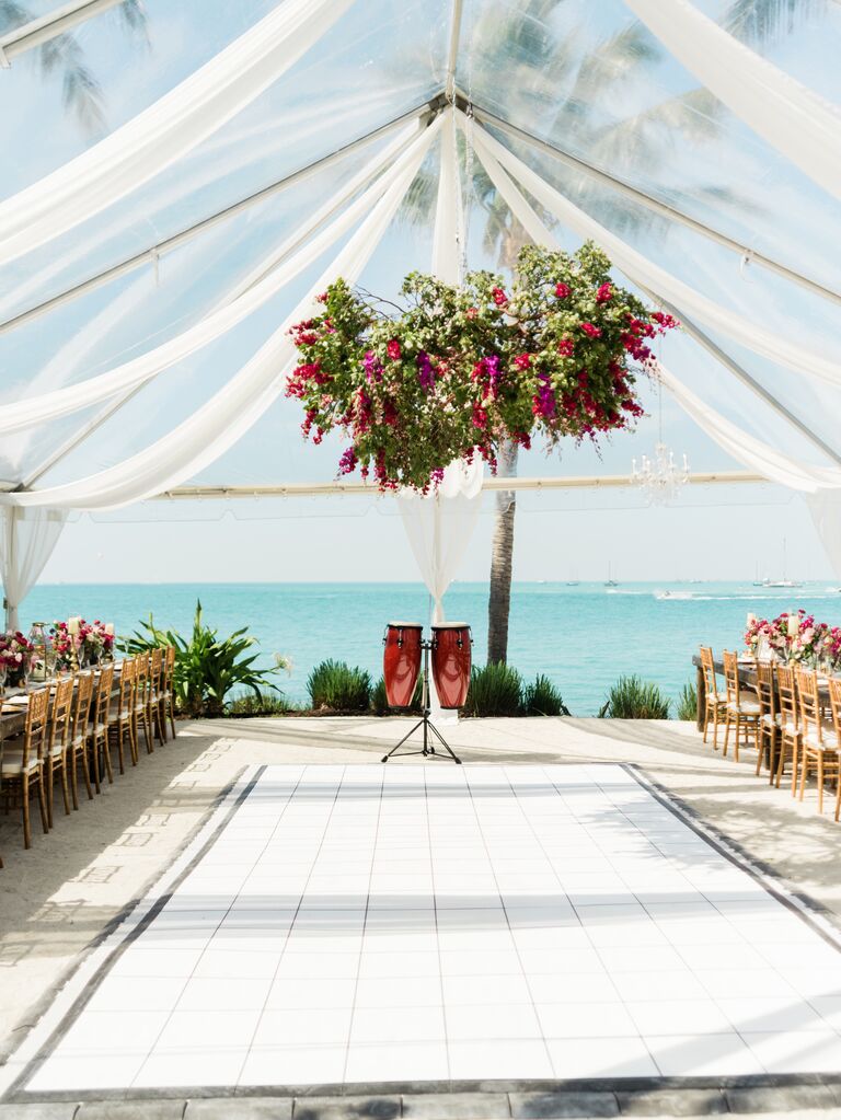 clear top wedding reception tent at oceanfront venue with colorful pink flower and greenery centerpiece hanging above the dance floor