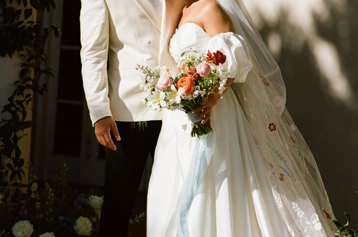 Bride Holding Bouquet of Pastel Flowers, Floral Embroidered Veil, Groom in White-and-Black Suit