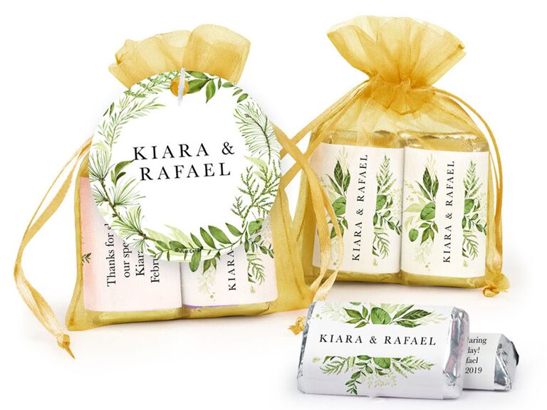 Gold drawstring bags holding custom chocolates, with white labels detailed with greenery and couple's names