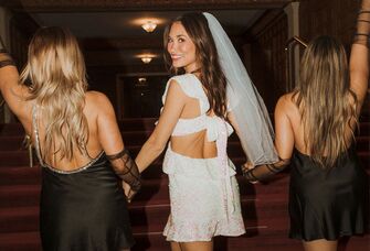 A bride walks hand-in-hand with two friends.