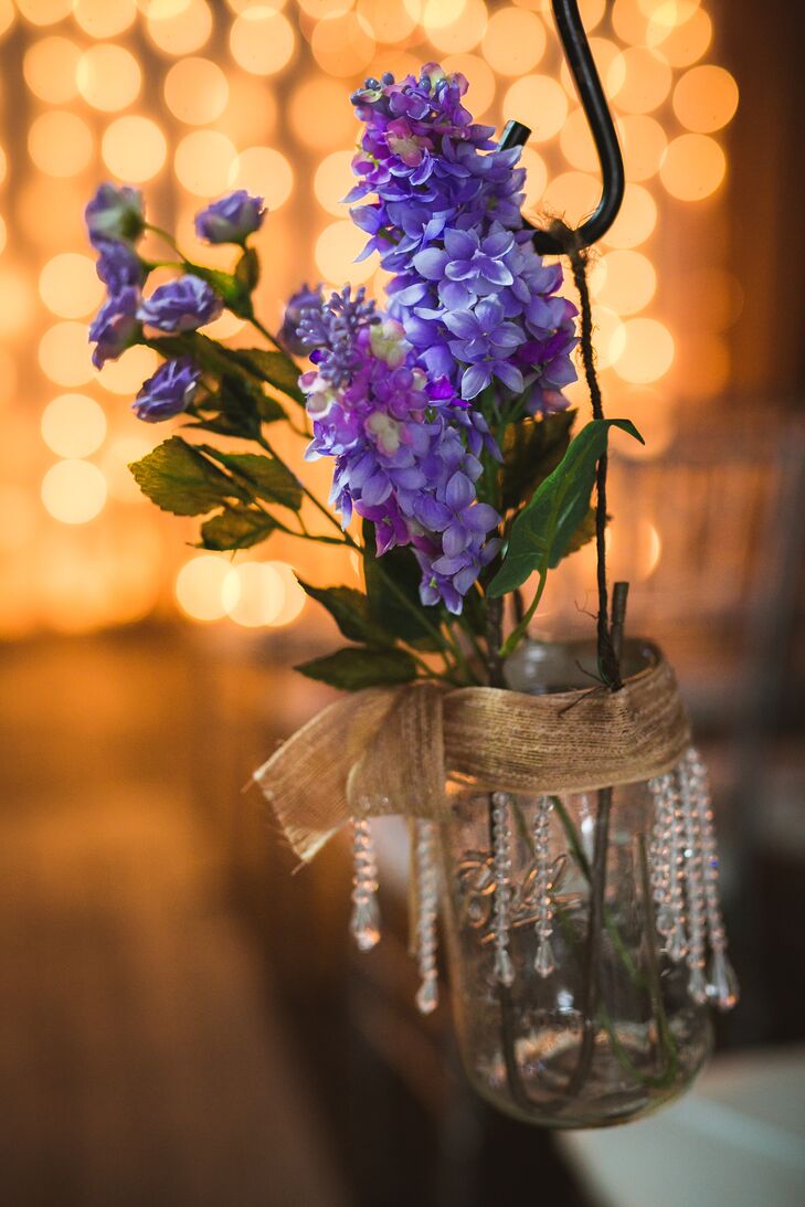Mason jars filled with purple wildflowers hung from chairs on the ceremony aisle. The mason jars were decorated with gold ribbon and crystals.