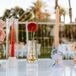 Unique geometric glass vases and colored candles with bold-colored, single-flower arrangements on the bar at a retro desert wedding reception in California.