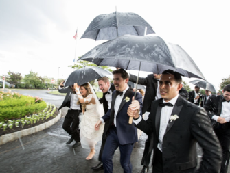 Bride, groom, and wedding party holding umbrellas and running for cover on rainy wedding day 