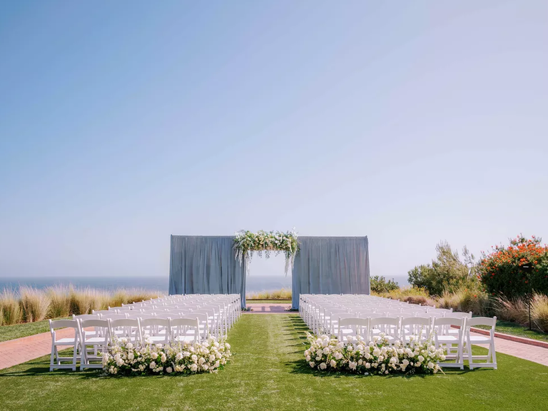 An outdoor wedding ceremony site with gorgeous white blooms and a floral archway.
