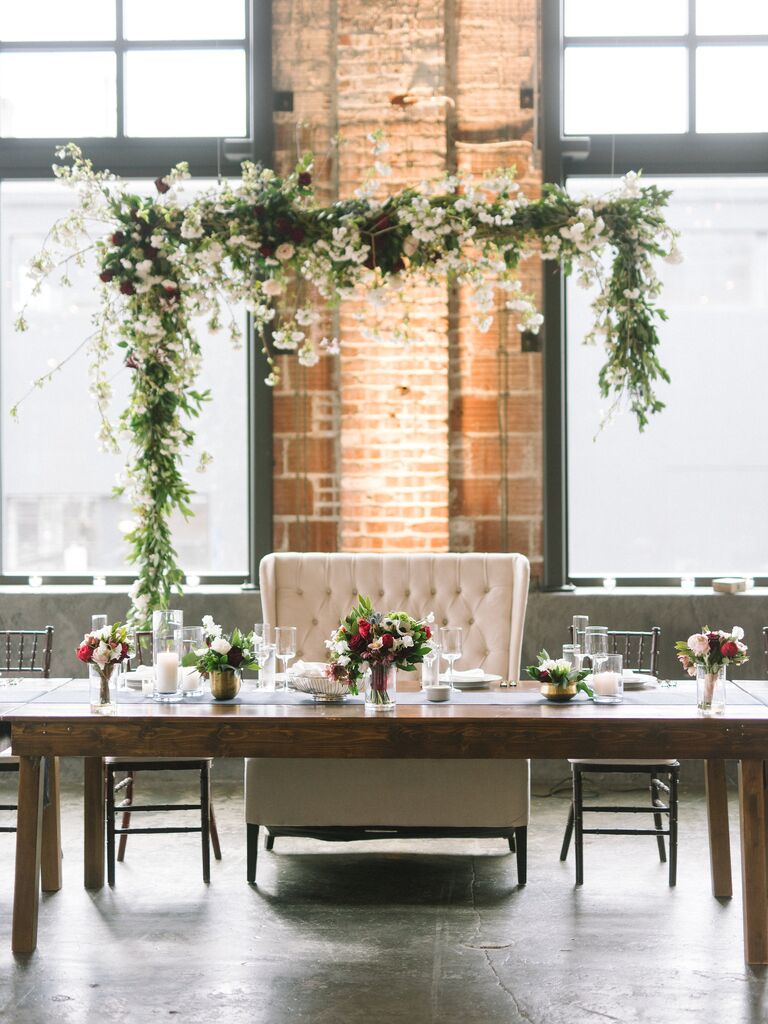 wedding sweetheart table with greenery garland and flower installation hanging against the wall behind loveseat